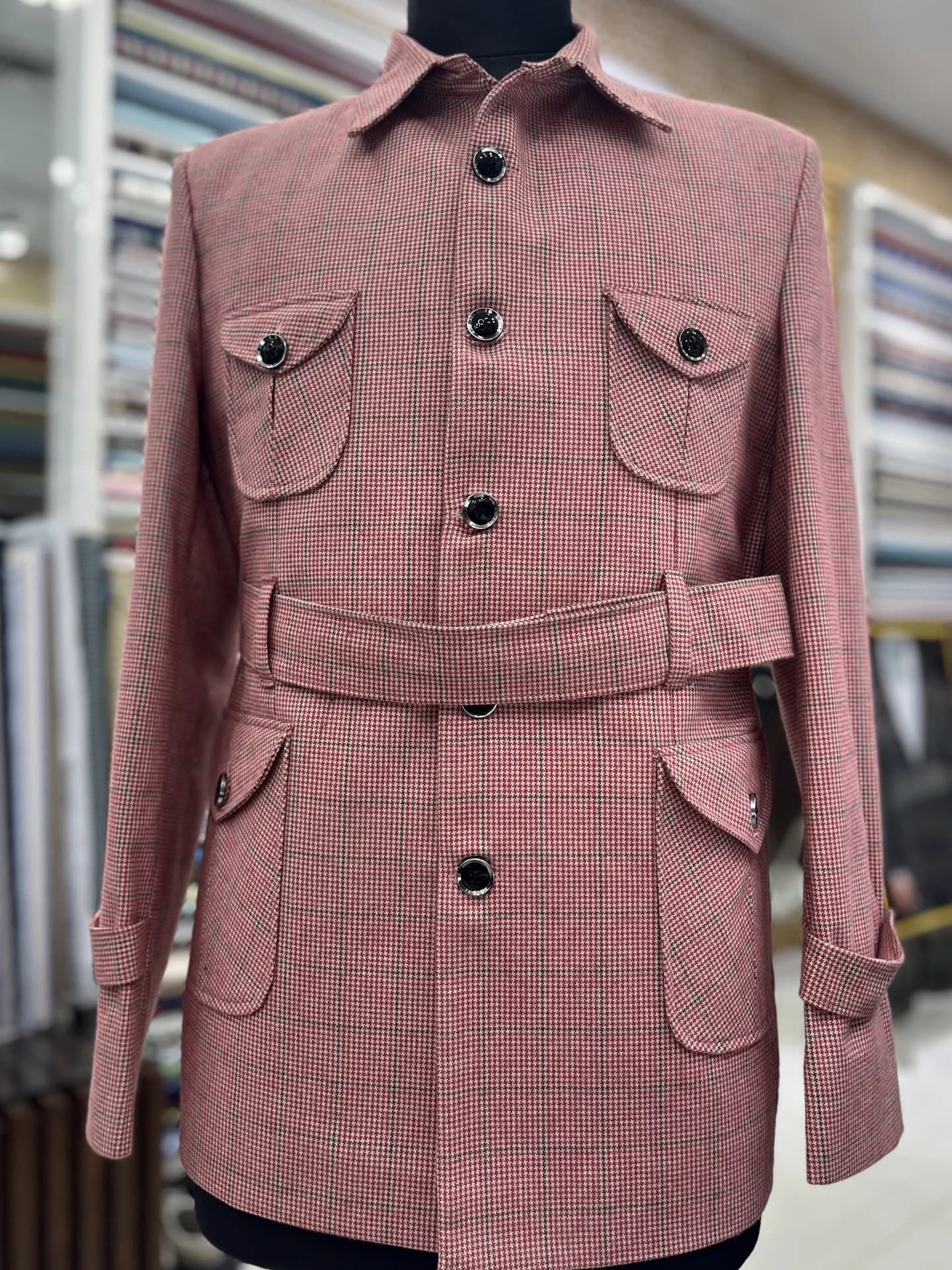 A belted houndstooth field jacket on the Punjab Fabrics floor, fabric bolts behind it.