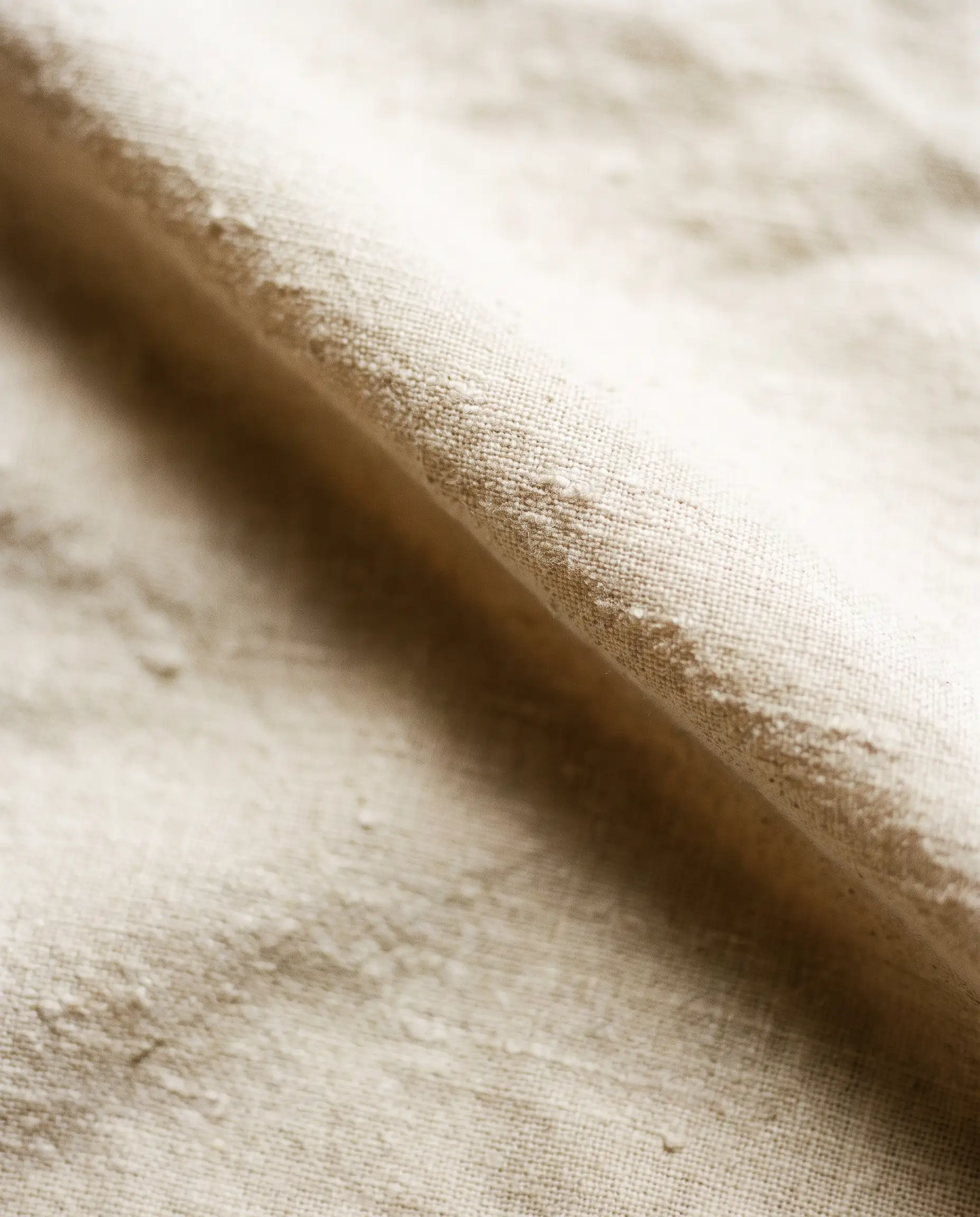 Ivory linen with visible slub texture and soft window-light across a natural fold.