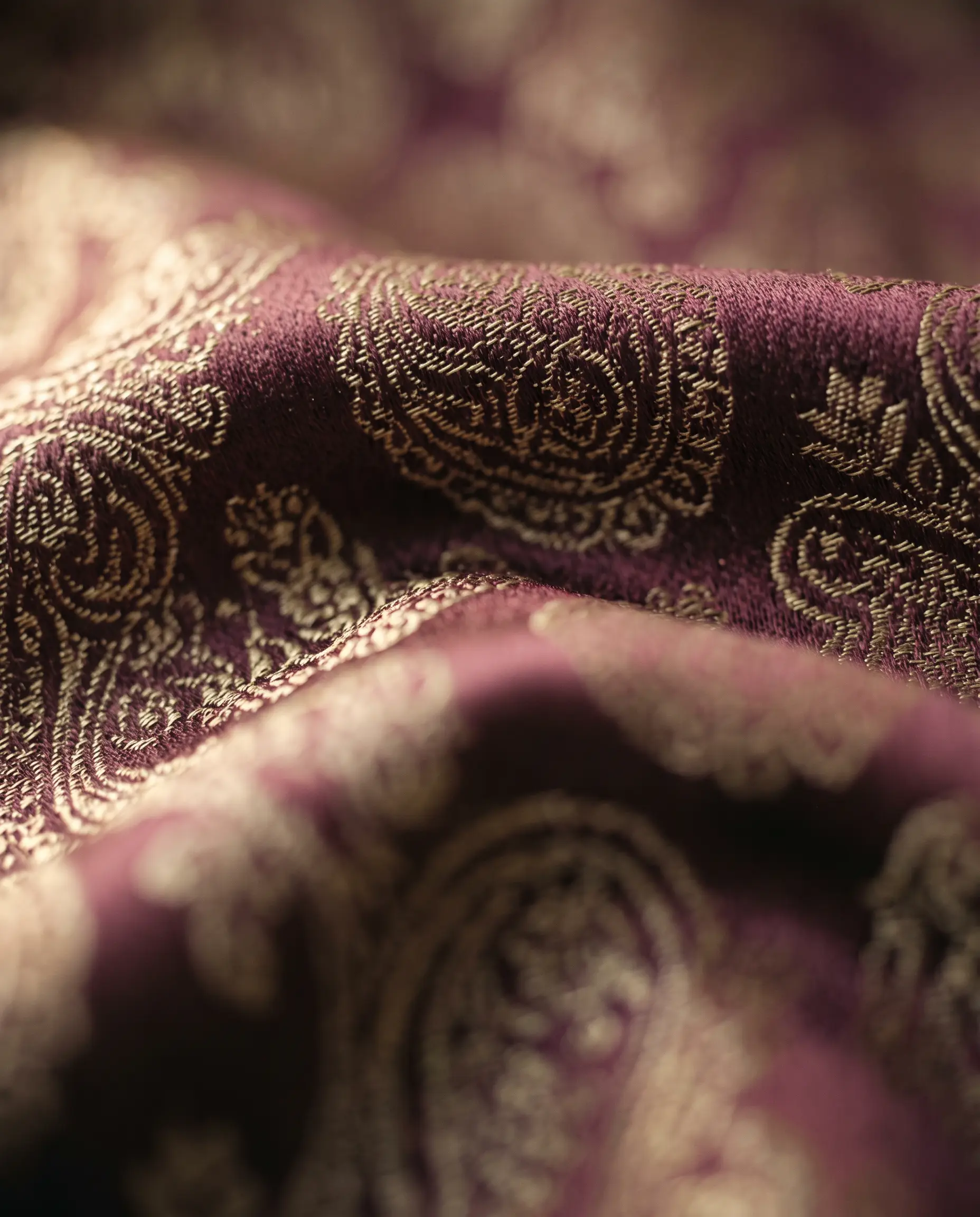 Deep burgundy silk brocade with fine gold paisley thread-work, catching warm side-light.